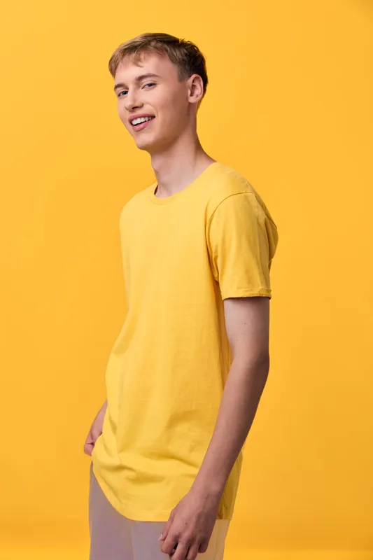 Young man in a bright yellow tee stands before a yellow backdrop, smiling and relaxed, showcasing casual style for lifestyle or fashion stock.