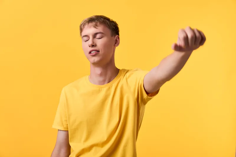 Youth relaxation stretching gesture with eyes closed against a yellow background, casual clothing, conveying calm energy and focus in a bright studio setting