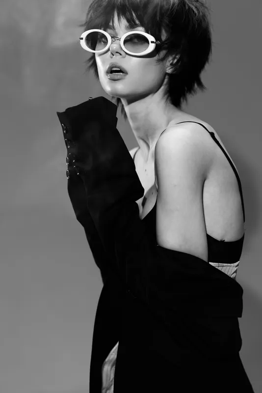 Black and white stylish woman wearing sunglasses and loose jacket with confident expression in studio lighting.