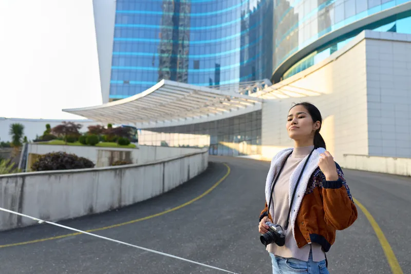 Urban scene with a woman holding a camera near sleek skyscrapers, city street and modern architecture, casual style, daylight photography, travel vibe