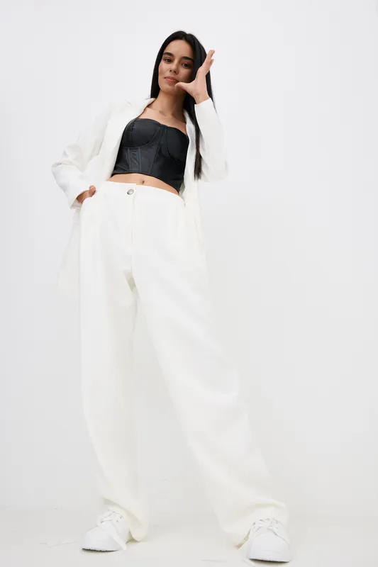 confident woman in white oversized suit and black crop top posing against white background, casual fashion style, modern look, youthful attitude