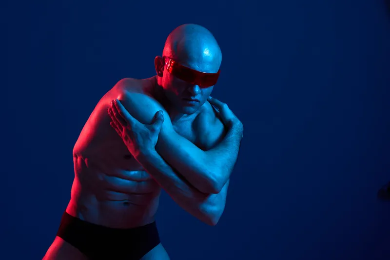 Strong man in a dynamic pose, showcasing muscular physique against a vibrant blue and red background, creating a striking visual contrast.