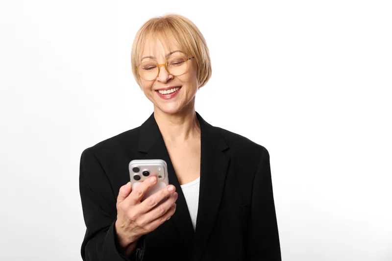 Woman business smartphone smiling blazer portrait communication technology, mature woman in black blazer holds phone and smiles, isolated studio portrait on white background