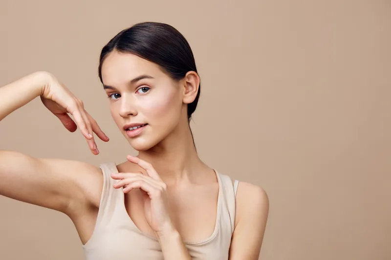 Beautiful young woman with smooth skin posing elegantly against a neutral background, showcasing confidence and natural beauty in a light beige outfit