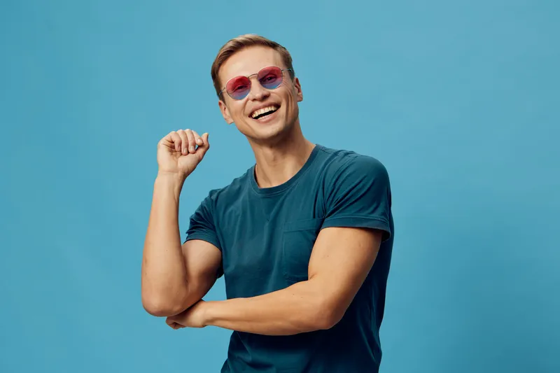 Smiling young man wearing sunglasses casual dark t-shirt posing blue background happy carefree lifestyle digital nomad concept