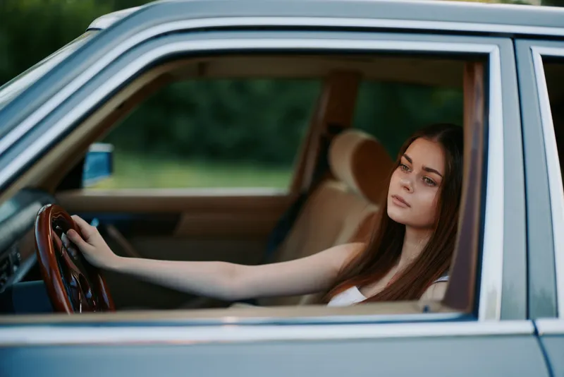 A young woman reflecting while sitting in a classic car, showcasing a thoughtful expression and vintage interior, perfect for automotive and lifestyle themes.