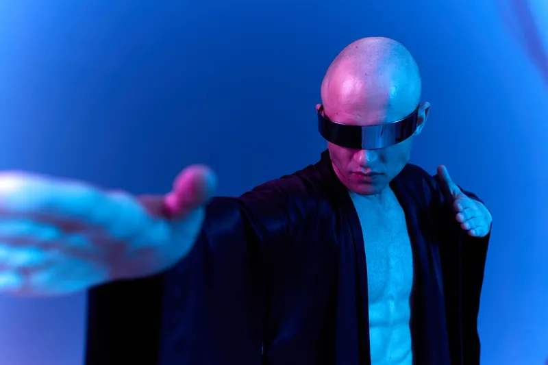A focused man dressed in black with sunglasses, exuding confidence in a vibrant blue background. This black and white image captures a strong, dramatic essence.