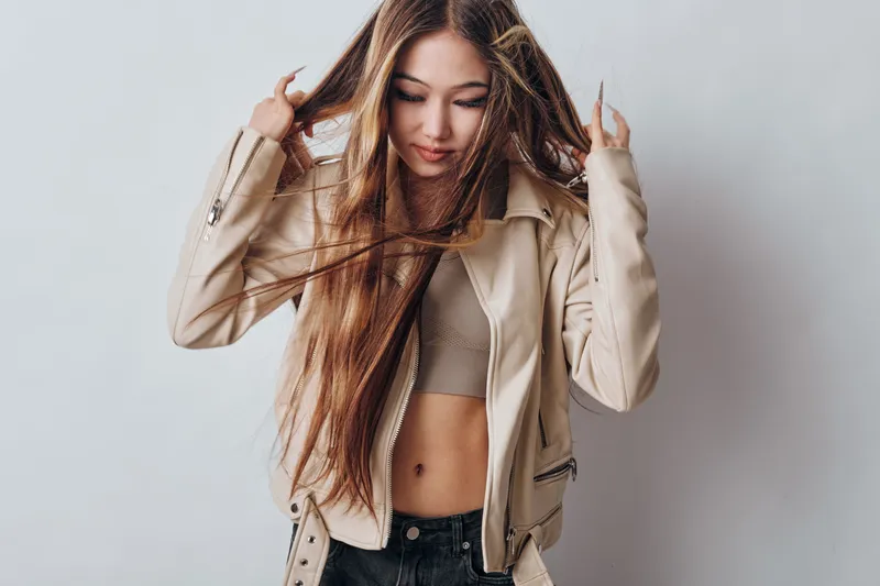 Woman with long hair wearing beige jacket and crop top posing on gray background. Fashion model with casual outfit and natural look for style, beauty, youth and confidence portrait.
