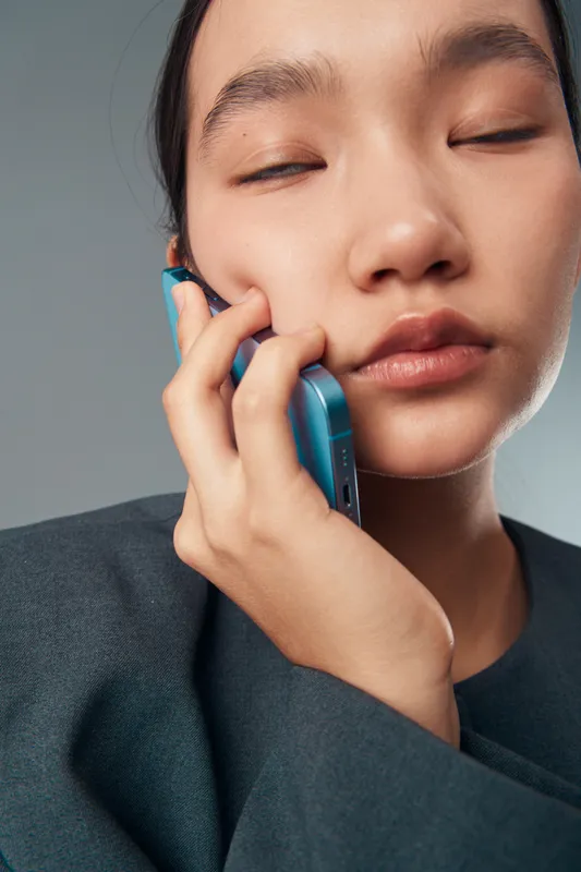 Closeup of woman with closed eyes holding smartphone to ear for communication, technology, connection, and mobile phone use in casual clothing on gray background with calm expression.
