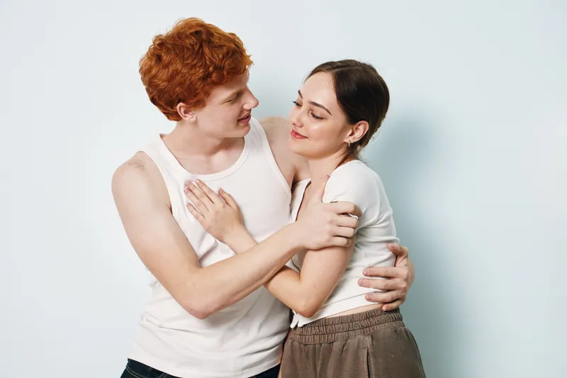 Young couple embracing and looking at each other, showing affection and connection. Casual clothing, studio background, relationship, love and intimacy between man and woman.