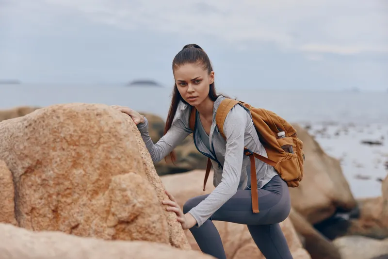 Young athletic woman exploring rocky coastline, wearing outdoor gear, displaying determination and focus, suitable for adventure and nature themes