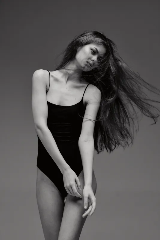Black and white portrait of a slender woman with long hair wearing a black bodysuit in elegant pose