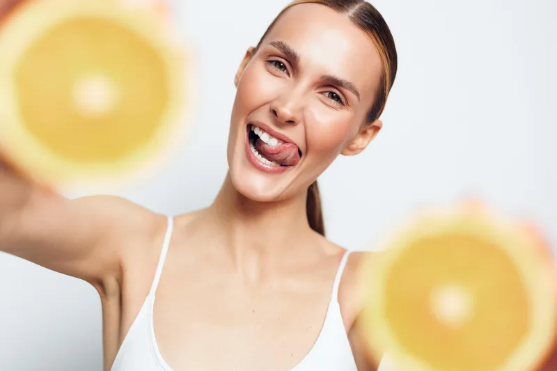 Smiling woman presents bright citrus fruits toward the camera, showcasing freshness, healthy lifestyle, and joyful mood on a clean background. Fresh energy enhances the scene. Today!