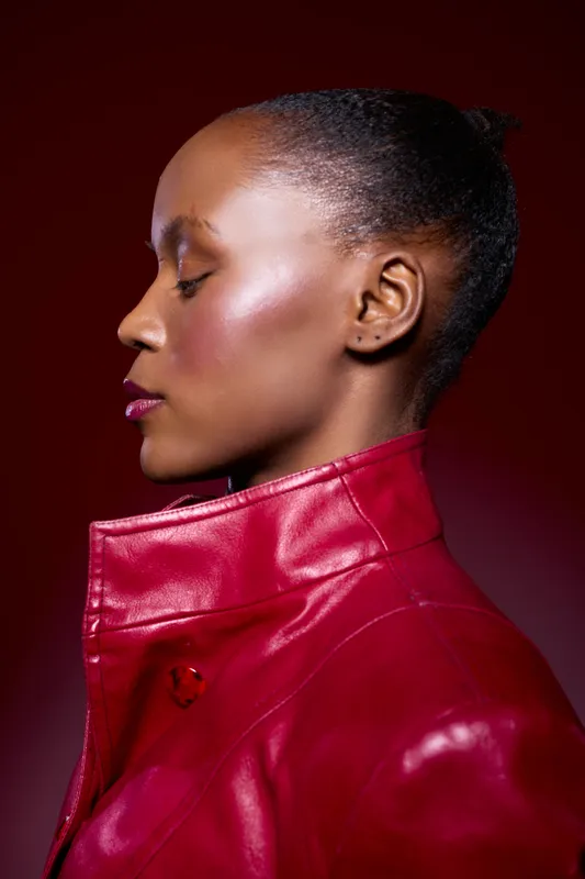 Profile of a black African woman with smooth dark skin wearing a red leather jacket. Studio portrait on dark red background. Concept for fashion, elegance, and beauty.