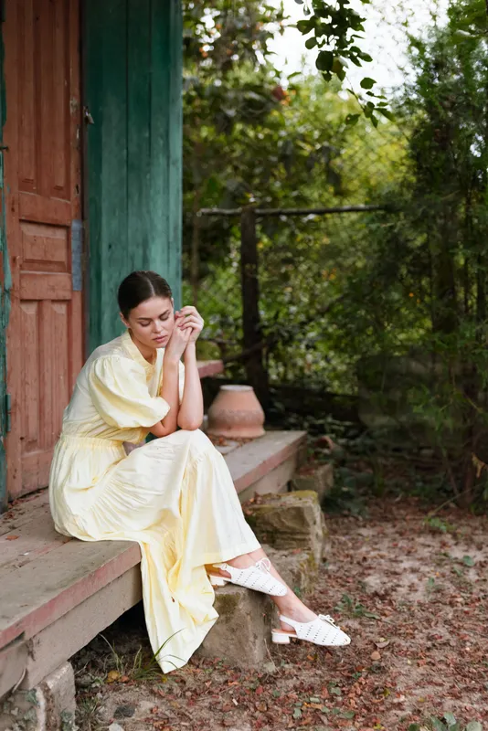 woman dress yellow outdoor garden serene peaceful sitting contemplative porch door nature calm sunlight fashion lifestyle alone relaxed moment environment greenery breeze rustic scene tranquil idle
