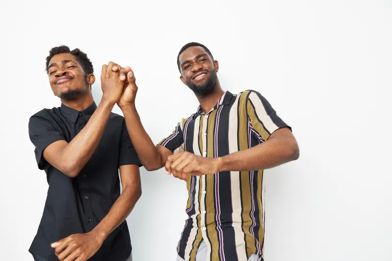 Two joyful African American men celebrate together, expressing happiness through their playful gesture. Dressed casually, they radiate energy and friendship.