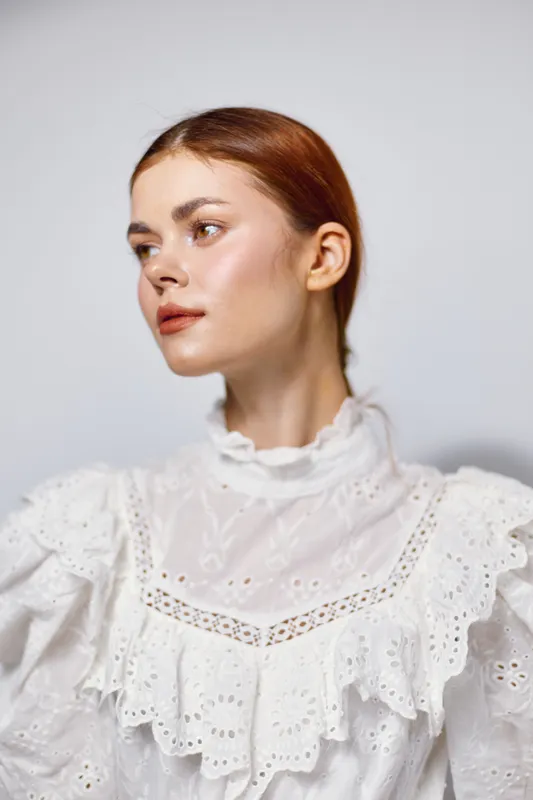 Elegant young woman in a white vintage dress, showcasing a calm expression against a soft neutral background, ideal for fashion and beauty concepts