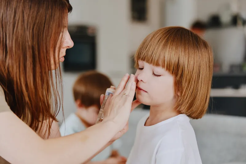 Caring woman applying skincare to her daughter, showcasing a moment of tenderness and affection in a cozy indoor setting with a warm atmosphere.