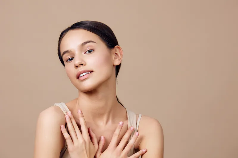 Natural beauty portrait of a young woman with smooth skin and subtle makeup, posing against a warm beige background, conveying femininity and confidence