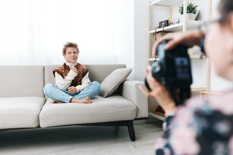 Authenticity shines in a candid portrait of a child seated on a sofa, conveying a playful school theme and simple lifestyle in warm daylight for viewers.