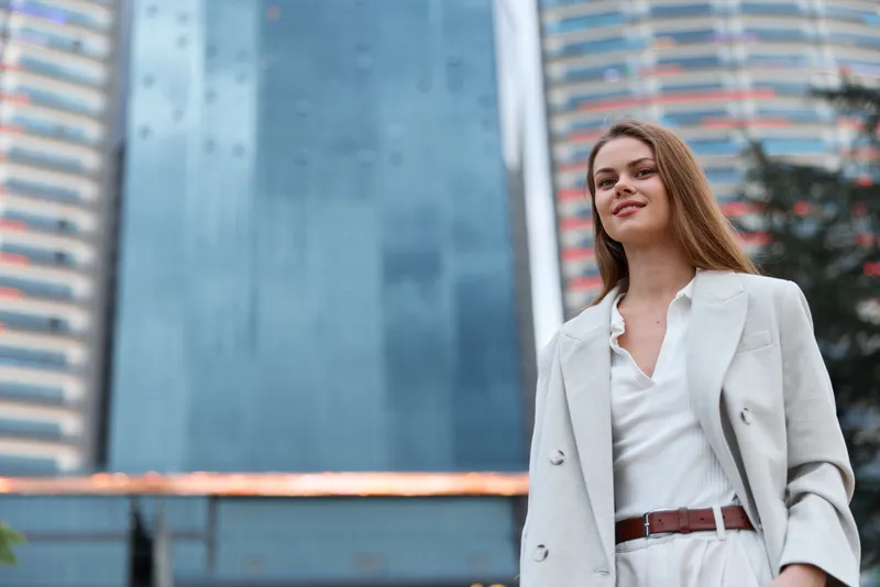 Confident business woman in a stylish suit standing in an urban setting, showcasing modern professionalism and elegance amidst a city backdrop.