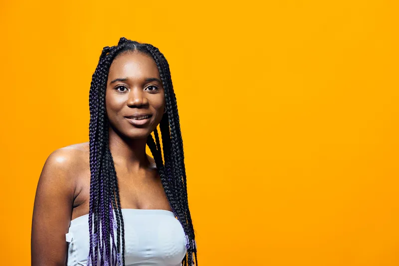 Young woman with braided hair smiling against vibrant orange background showcasing beauty, confidence, and style Perfect for youth culture and fashion imagery