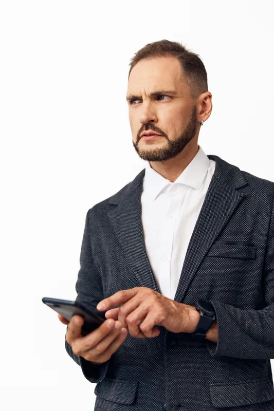 An focused business professional man holds a smartphone, standing against an isolated colored background, showing determination, confidence, and calm concentration.