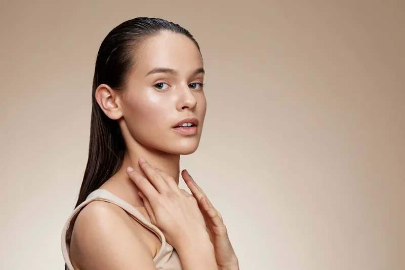 Elegant model with wet hair posing against a neutral background, showcasing natural beauty, confidence, and polished skin Ideal for fashion and beauty themes