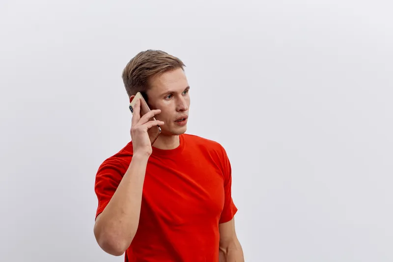 Young caucasian man talking on mobile phone wearing red t-shirt isolated on white background communication technology digital nomad concept