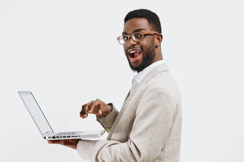 Smiling man with glasses holding a laptop, dressed in beige blazer and white shirt, posing studio portrait on plain white background. People business technology concept