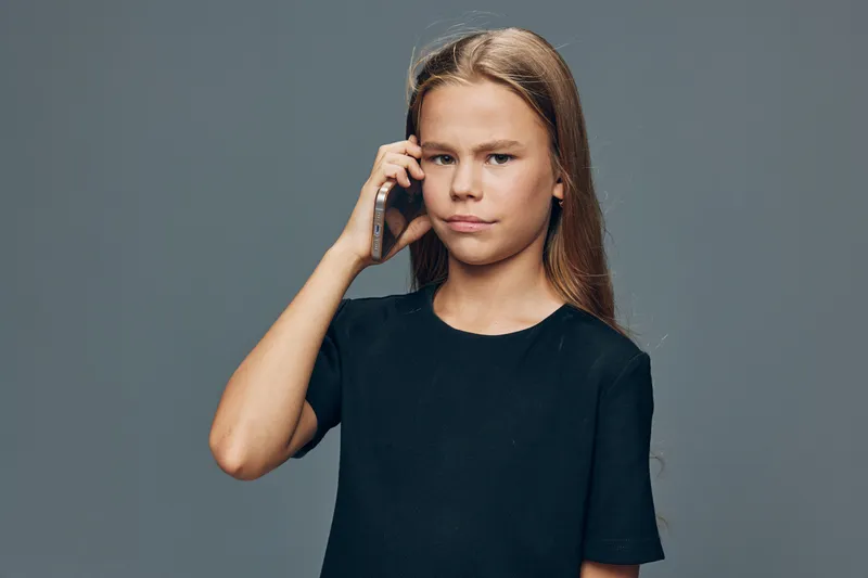 Girl using smartphone for communication in studio with gray background, serious facial expression, casual clothes and natural light for technology usage and connection.