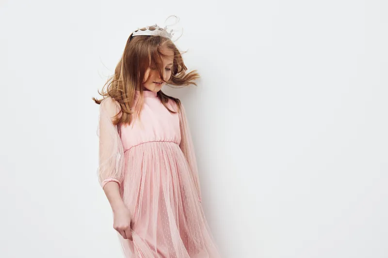 A young girl in a pink dress twirls playfully against a simple white background, showcasing joy and innocence Perfect for children s fashion and playful themes