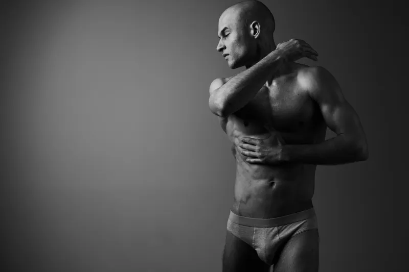 Black and white image of a man posing gracefully, showcasing his athletic physique and strong emotion for dramatic effect. Perfect for health and fitness themes.