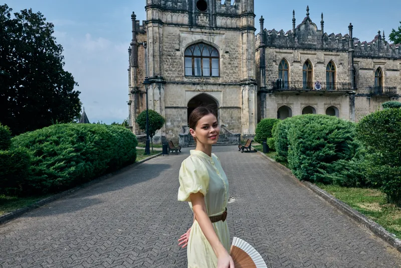 Woman in vintage dress smiling with hand fan in front of historic building, authenticity inclusivity