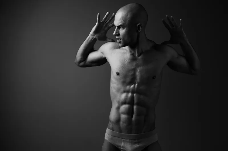 Black and white portrait of a strong man showcasing his muscular physique, captured in an artistic pose with dramatic light and shadows enhancing the mood.