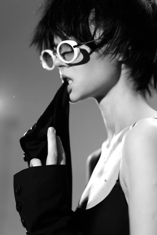 Black and white portrait of a stylish woman with short hair wearing round sunglasses and biting clothing fabric