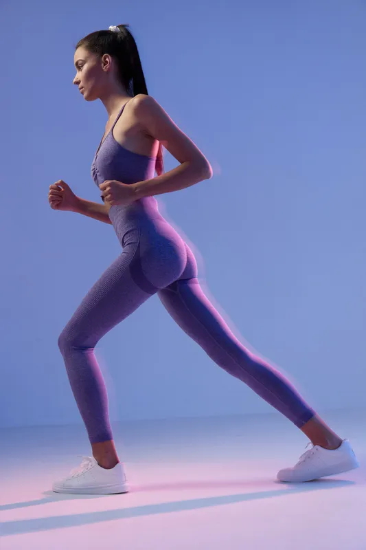 Woman sport fitness training in purple activewear, demonstrating strength and focus in a modern studio with dynamic lighting and a clean background.