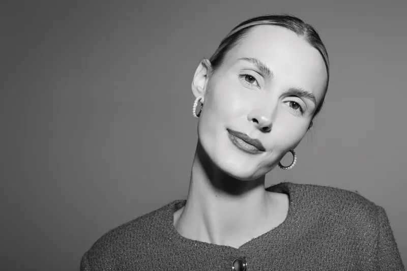 Portrait of a fair skinned Caucasian woman with slicked back hair wearing hoop earrings and a textured sweater in monochrome lighting.