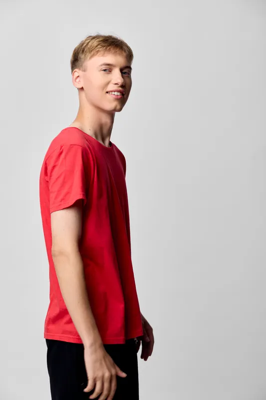 Young man in a red shirt stands in a studio, presenting casual fashion and confident posture with a light smile, ideal for lifestyle and stock photo projects.