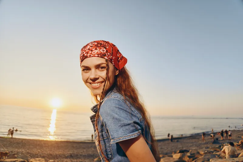 lifestyle woman in modern boho-western denim street style smiling at sunset on beach with warm film color tones, casual and relaxed atmosphere