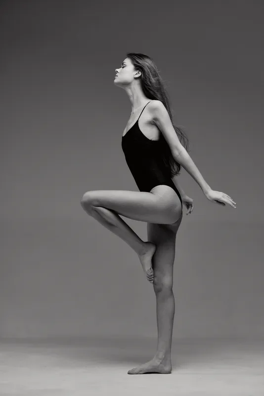 Black and white image of a graceful woman dancer posing in a leotard with elegance and balance in a studio setting.