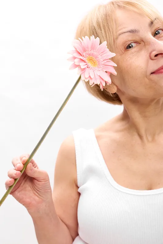 Woman closeup portrait holding pink gerbera flower, spring mood, soft light, gentle smile, relaxed posture, white background, minimal studio scene