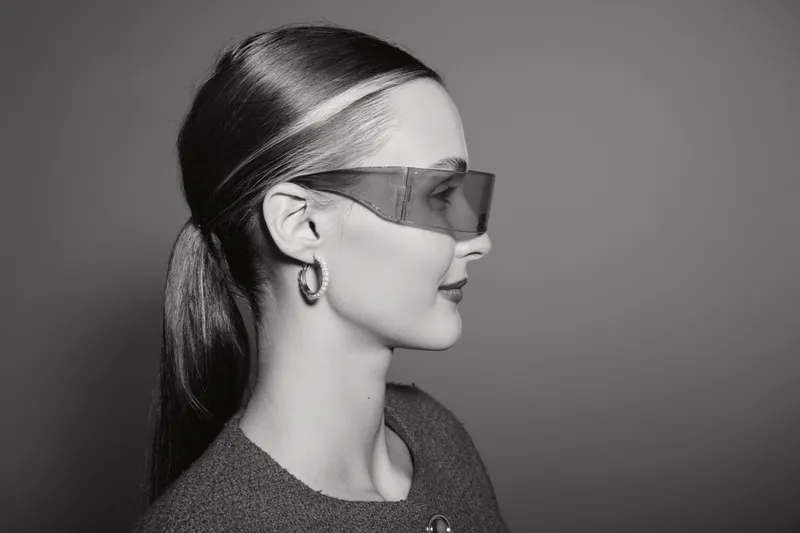 Profile of white woman with light skin wearing futuristic sunglasses and hoop earrings in studio. Concept of fashion and style.
