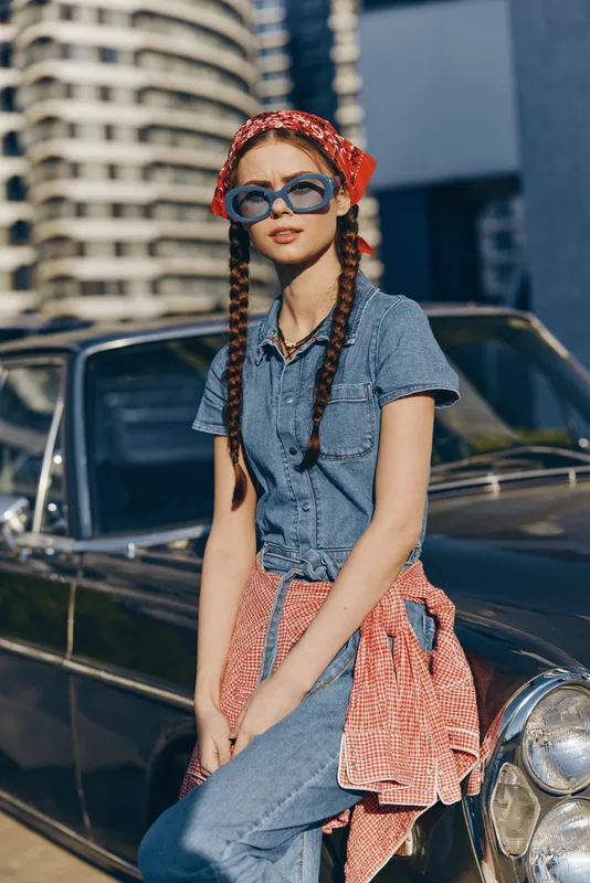 Lifestyle woman in modern boho-western denim street style with red bandana and sunglasses, casual urban fashion, film color in sunny city setting.