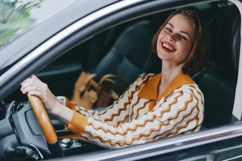 Smiling woman in the driver seat, hands on the steering wheel, enjoying a bright day.