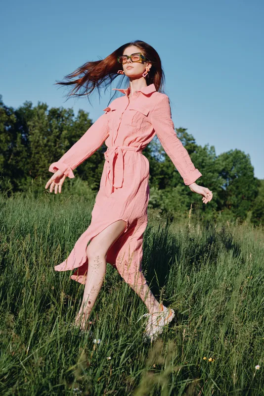 Young woman in a pink dress walking through a lush green field, showcasing carefree emotions and a sense of freedom in nature during a sunny day