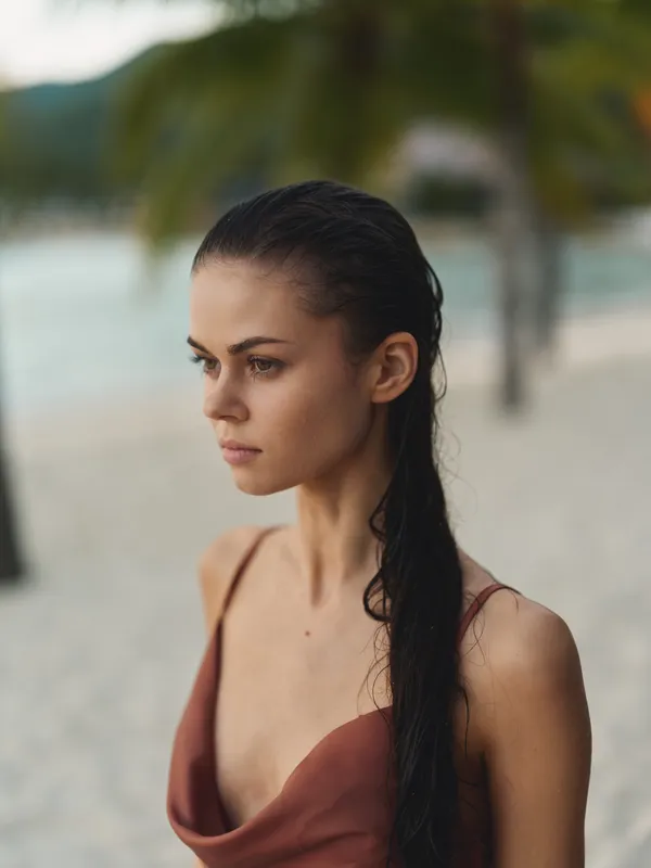 Young woman with long dark hair standing on tropical beach wearing brown dress, thoughtful expression, warm natural lighting, summer vacation mood.