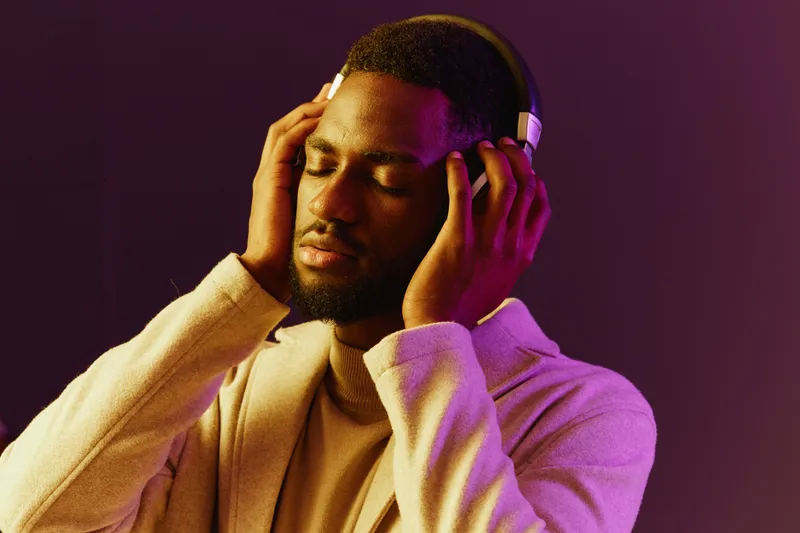 Young Black man enjoying music with headphones in a stylish outfit, conveying relaxation and joy with a colorful gradient background