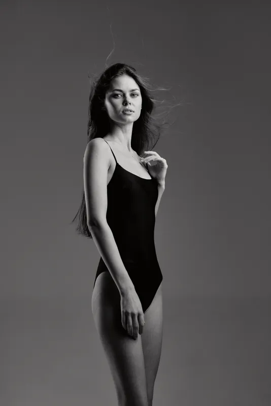 Black and white portrait of a young woman in a black swimsuit with serious expression in studio lighting.