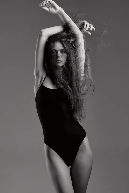 Black and white artistic portrait of a slender woman with long hair posing in a bodysuit expressing grace and style.